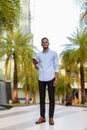 Full length shot of handsome black African businessman outdoors in city during summer smiling and holding phone Royalty Free Stock Photo