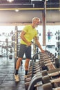 Full length shot of a happy athletic mature man in sportswear taking a dumbbells, looking in a big mirror and smiling