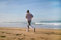 A slim athletic young woman in sportswear running on the Atlantic beach, leaving footsteps in the wet sand Royalty Free Stock Photo