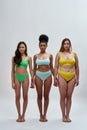 Full length shot of three multiethnic women with different body shapes in colorful underwear holding hands, standing