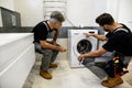 Full length shot of two repairmen, workers in uniform working, reading washing symboles on washing mashine before fixing