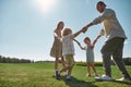 Full length shot of young parents holding hands in circle with their two little kids, boy and girl in green park on a Royalty Free Stock Photo