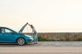 Full length shot of young woman looking under the hood of her broken car, trying to repair it on her own while standing Royalty Free Stock Photo