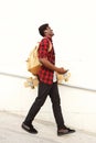 Full length side of handsome young african american male student with skateboard and bag walking outdoors Royalty Free Stock Photo