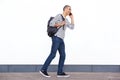 Happy young man walking with bag and talking on mobile phone against white wall Royalty Free Stock Photo