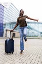 Full length side portrait of a traveling young woman with mobile phone and suitcase at airport terminal Royalty Free Stock Photo