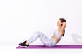 Full length side view athletic woman in white tights and top lying on mat and training doing sit ups, exercising abdominal muscles