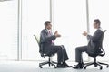 Full-length side view of businessmen discussing while sitting on office chairs by window Royalty Free Stock Photo