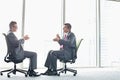 Full-length side view of businessmen discussing while sitting on office chairs by window Royalty Free Stock Photo