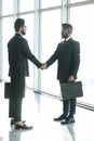 Full length side view of businessmen shaking hands in airport terminal Royalty Free Stock Photo