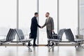 Full length side view of businessmen shaking hands in airport terminal Royalty Free Stock Photo