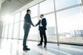 Full length side view of businessmen shaking hands in office windows. Royalty Free Stock Photo