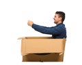 Full length side view of childish man sitting inside a cardboard box pretending to drive a new car isolated over white background