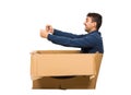 Full length side view of childish man sitting inside a cardboard box pretending to drive a new car isolated over white background