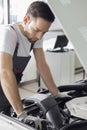 Full length side view of male mechanic examining car engine in repair shop Royalty Free Stock Photo