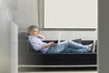 Full-length side view of Middle-aged man using laptop while lying on sofa Royalty Free Stock Photo