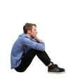 Full length side view of upset and tired boy teenager sitting on the floor keeps hand under chin looking ahead thoughtful isolated Royalty Free Stock Photo