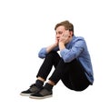 Full length side view of upset and tired boy teenager sitting on the floor keeps hands under chin looking down thoughtful isolated