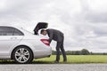 Full length side view of young businessman looking in car trunk at countryside