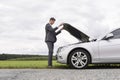 Full length side view of young businessman opening broken down car hood at countryside Royalty Free Stock Photo