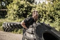 Full length side view of young man athlete flipping large tire outside gym Royalty Free Stock Photo