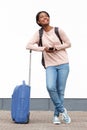 Full length smiling young african american woman standing with suitcase and mobile phone against white wall Royalty Free Stock Photo