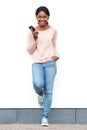 Full length smiling young black woman standing against white wall with cellphone Royalty Free Stock Photo