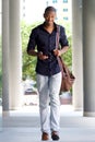 Full length smiling young man walking in city with mobile phone and bag Royalty Free Stock Photo