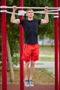 Young strong man does pull-ups on a horizontal bar on a sports ground in the summer in the city. Royalty Free Stock Photo