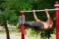 Young strong man does pull-ups on a horizontal bar on a sports ground in the summer in the city. Royalty Free Stock Photo