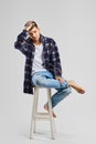 Full length studio portrait of young bold man in shirt and jeans sitting on tall wooden chair Royalty Free Stock Photo