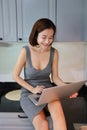 Full length stunning asian housewife, short hair in grey dress reading recipe from computer while sitting in kitchen counter with