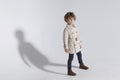 Full length of a stylish adorable curly little boy, wear in a trench, poses in studio, white background.