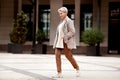 Full length stylish woman walking Street and wears trendy business clothes outfit, oversize jacket, tie, pants and white Royalty Free Stock Photo