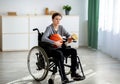 Full length of teen basketball player in wheelchair holding ball and trophy, feeling sad over his injury at home