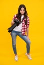 Full length of teen girl with dslr professional photo camera with big photo lens. Kid photographer isoalted on yellow Royalty Free Stock Photo