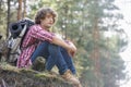 Full length of thoughtful male backpacker relaxing on cliff in forest