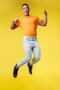 Full-length vertical shot cheerful masculine hipster guy in trendy orange t-shirt, white pants, jumping from happiness