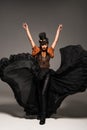 Length view of attractive steampunk woman in top hat with goggles standing with hands up on grey