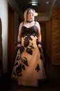 Full length view of a blonde female model, dressed in a black and white queen dress in dark corridor. Mysterious