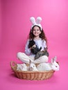 Full length of a pretty little girl with white bunny ears, showing basket with little rabbits, isolated pink background. Royalty Free Stock Photo