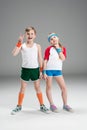 Full length view of cute smiling boy and girl in sportswear standing together and gesturing isolated on grey Royalty Free Stock Photo