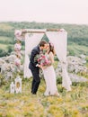 The full-length view of the kissing newlyweds near the lovely decorated arch during the wedding ceremony in the Royalty Free Stock Photo