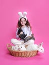 Full length of a pretty little girl with bunny ears, showing straw basket with little rabbits, on a pink background. Royalty Free Stock Photo