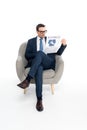 full length view of serious businessman in eyeglasses reading newspaper while sitting in armchair Royalty Free Stock Photo