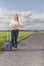 Full length of woman hitching while holding anywhere sign on country road