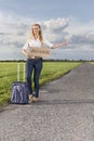 Full length of woman hitching while holding anywhere sign on countryside