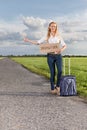 Full length of woman hitching while holding anywhere sign on countryside