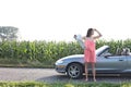 Full length of woman shielding eyes while holding map by convertible