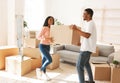 Full length of young black man with his girlfriend carrying cardboard box in their new home on moving day Royalty Free Stock Photo